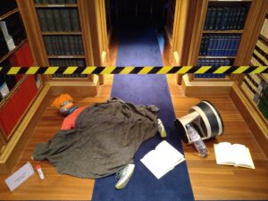 A dummy lies on the ground behind some hazard tape, with a kick step lying on its side and a container of tablets next it